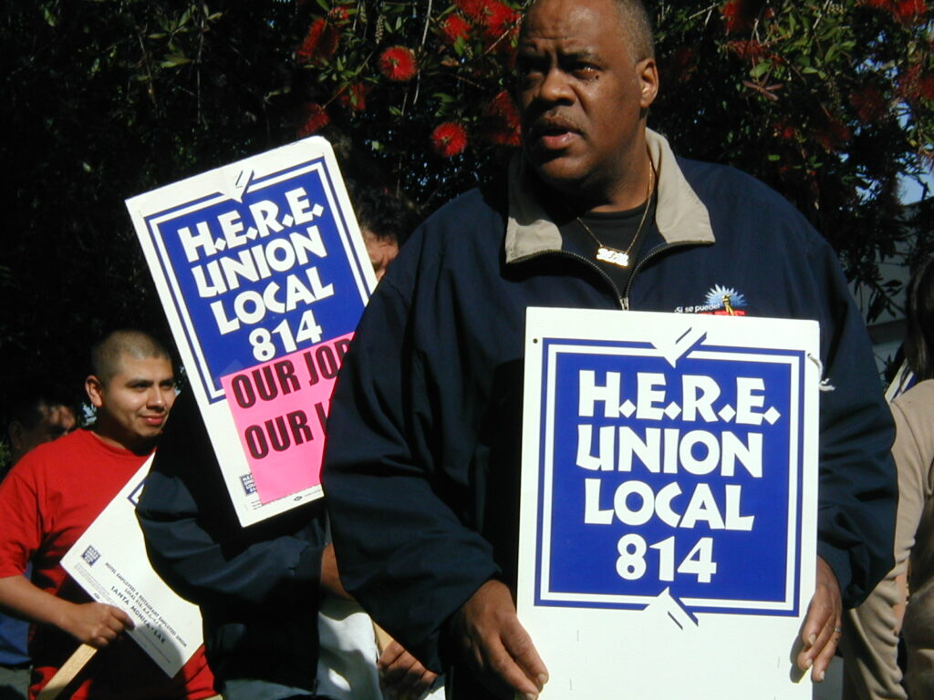 Workers on the picket line holding signs reading "H.E.R.E. Union local 814"