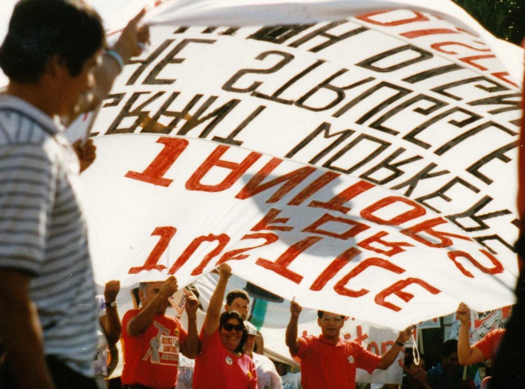 A group of workers lifts a large, red, white, and black Justice for Janitors banner up like a parachute at a march.